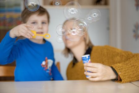 Kind spielt mit Seifenblasen, Therapeutin hält die Flüssigkeitsdose