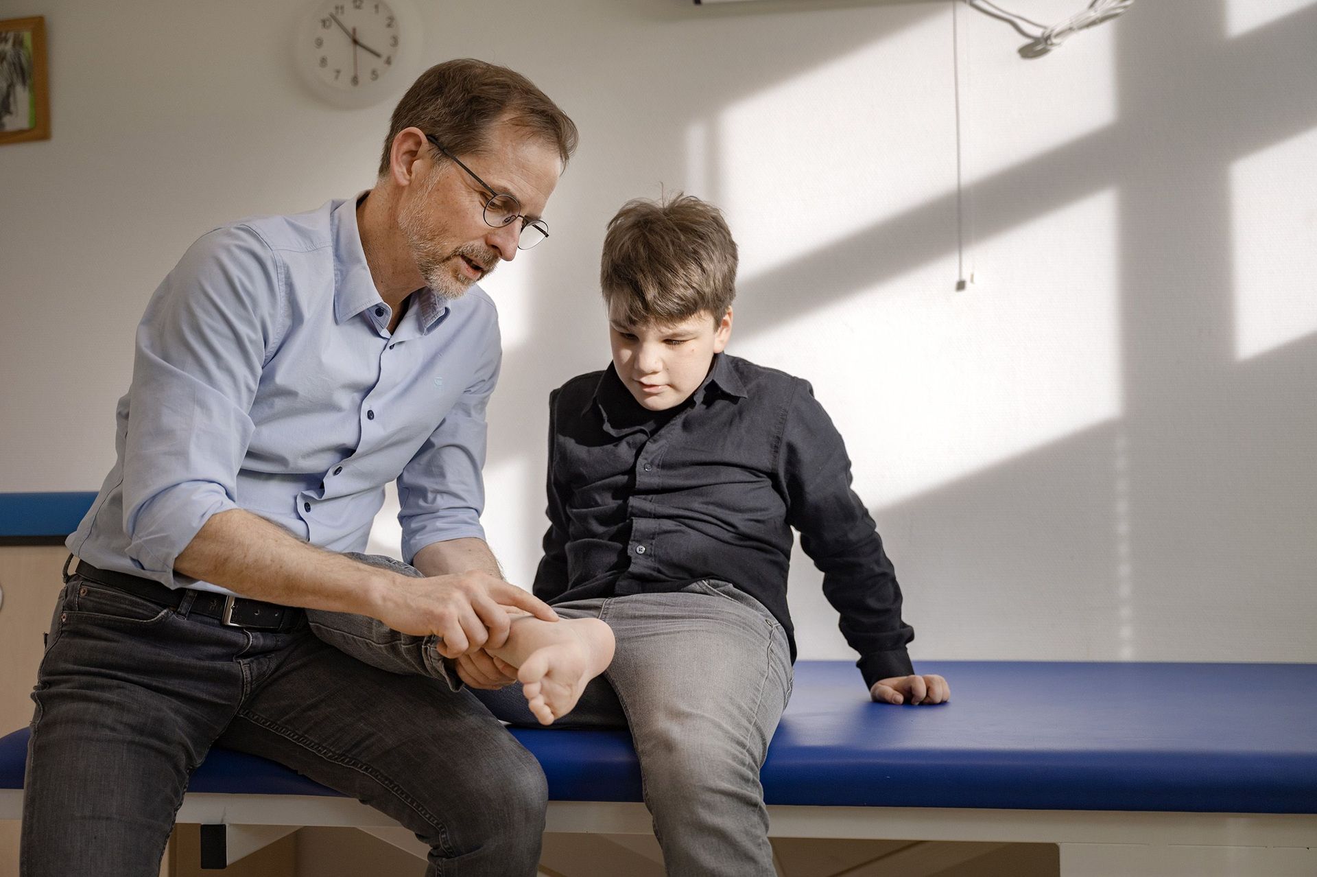 Arzt erklärt einem sitzenden Jungen etwas an seinem Fußgelenk
