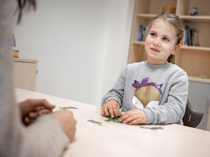 Kind sitzt am Tisch und spricht mit einer Therapeutin
