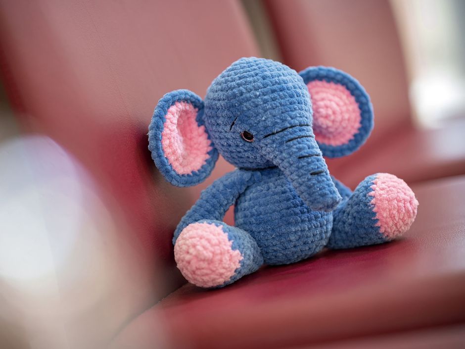 Kleiner Stofftier-Elefant sitzt auf einem roten Stuhl